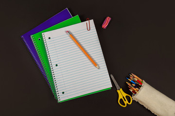 School supplies, notebooks, colored pencils, scissors on black table.