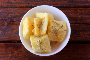 boiled and fried cassava (mandioca) in ceramic bowl on rustic wooden table