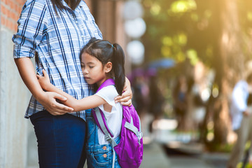 Back to school. Cute asian pupil girl with backpack hugging her mother with sadness before go to...