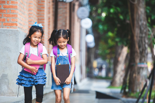 Back to school. Two cute asian child girls with school bag holding book and walk together in the school