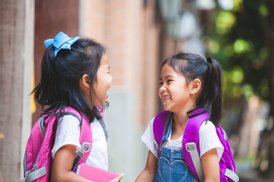 Back to school. Two cute asian child girls with school bag holding a book and talking together in the school