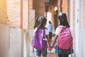 Back to school. Two cute asian child girls with school bag holding hand and walk together in the school