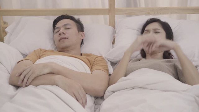 Asian couple wife annoyed Snore's husband when their sleep in bedroom, couple lying on bed at home female insomnia and can't sleep. Couple sleep at home concept.