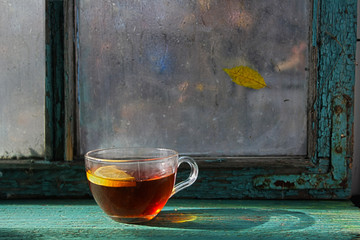 Hot cup of black tea with lemon on the wooden window sill. Autumn still life. It is raining outside the window. Rustic style - 272559441