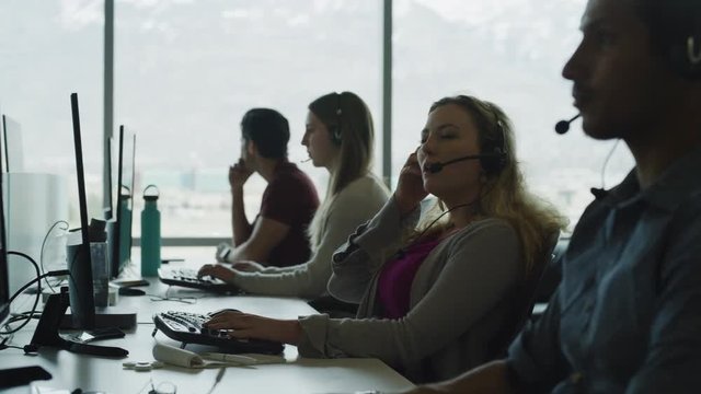 Tired customer service representative removing headset and rubbing face in call center / Pleasant Grove, Utah, United States