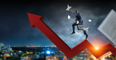 Black businessman climbing on red zigzag increasing arrow surrounded by flying papers on a dark storm cloudy cityscape background