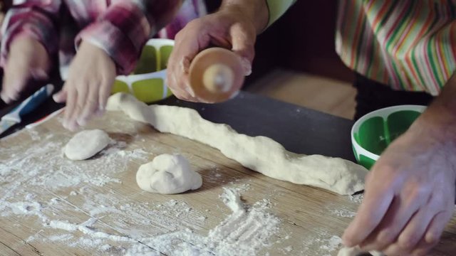 Close-up of the hands of children, two girls, whose dad teaches how to make kneading dough. Children in the kitchen with a wooden rolling pin for rolling dough, their hands in flour.