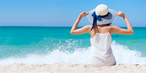 Summer time woman vacation on the beach. Cheerful woman wear summer dress and straw hats sitting on the beach look at sea. Time to relax in summer lifestyle outdoor shot on tropical island beach. © aFotostock