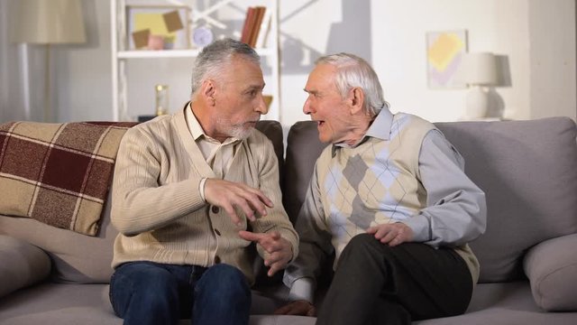 Old man explaining something to deaf friend, sitting on sofa at home, problems