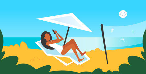 bikini woman sunbathing on sea beach girl in swimsuit using smartphone lying on sun lounger under umbrella summer vacation concept seaside background horizontal full length flat