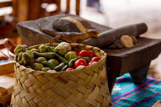a mexican handmade basket with green tomato, chila and several ingredients for mexican food, metate