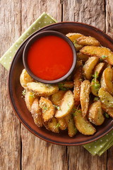 Hot potato wedges with parmesan cheese and oregano with pepper sauce close-up on a plate. Vertical top view