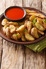 Delicious baked potato wedges with parmesan and oregano, served with pepper sauce close-up on a plate. vertical