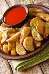 Homemade potato wedges with parmesan and oregano, served with spicy sauce close-up on a plate. vertical