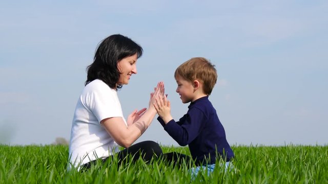 Happy family: mother and child sit on green grass and play, slapping each other on Batty