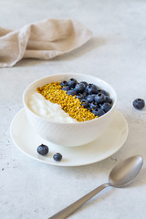 Bowl of greek yogurt, bee pollen and fresh berries on white stone background