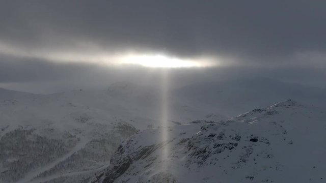Snowy mountains in low light through clouds while snowing. Wide shot. Drone moving forward and down