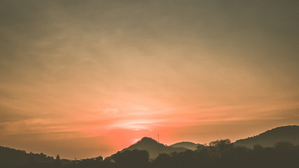 Sunset landscape with orange sky, silhouettes of mountains, hills and trees and lake