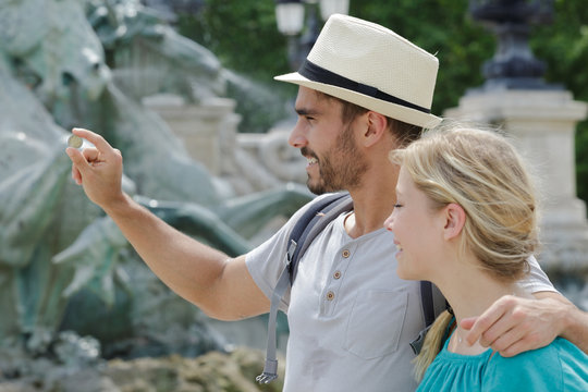 couple of tourists throwing coins in trevi fountain water