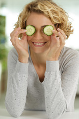 cheerful young woman covering her eyes with slices of cucumber