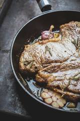 Grilled T-bone steak on the frying pan with garlic and rosemary. Selective focus. Shallow depth of field.