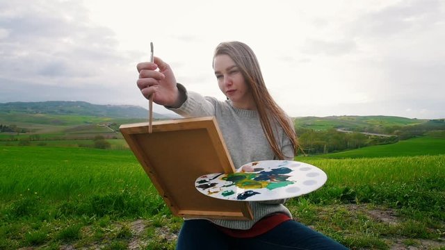 A young talanted woman sits on the meadow and draw - Measures image proportions