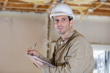 male builder or manual worker in helmet writing on clipboard