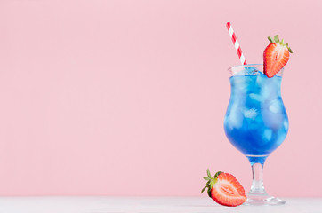 Alcohol juicy fruit blue cocktail with curacao liquor, strawberry slice, ice cubes, straw in frozen...