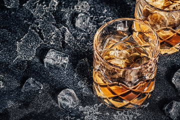Whiskey with ice on stone dark background.