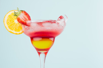Fresh alcohol striped cocktail with red and yellow liquor, orange slice, strawberry, ice on elegant...