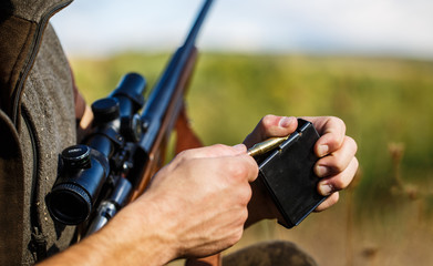Man is charging a hunting rifle. Male hunter in ready to hunt. Closeup. Ammunition with a gun,...