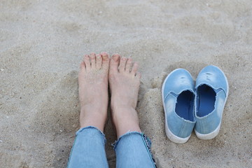 feet on the sand and a pair of shoes