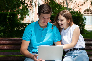 Happy young couple using laptop computer sitting on bench in city outdoor - Concept of relationship and people addicted to technology