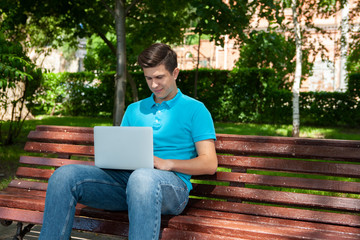 Obraz premium Young man university student online learning via laptop computer, sitting on a bench on a campus.