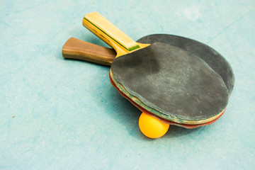 Ping pong paddles and ball on retro  blue wooden background. Rackets ruined by time