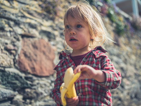 Little toddler eating banana outdoors