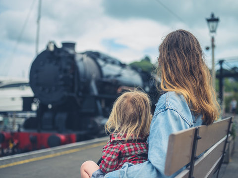 Young mother and toddler on bench watching steam train arrive