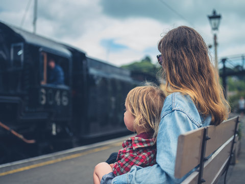 Young mother and toddler on bench watching steam train arrive