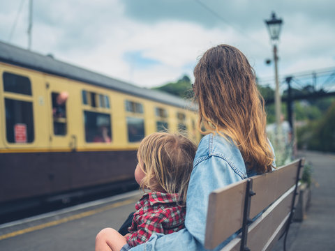 Young mother and toddler on bench watching train arrive