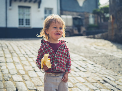 Little toddler eating banana outdoors