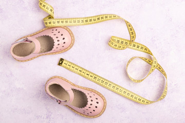Summer Pink Baby girl shoes and Yellow measuring tape on violet marble background. Top view trendy leather sandal, flat lay. Copy space for your text