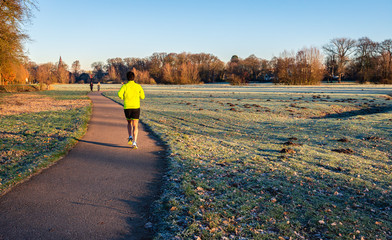 Unidentified woman in sportswear runs across a path in the park