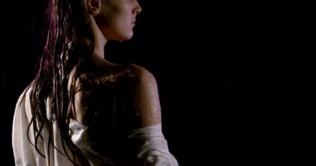 alluring young female is standing under rain in night, back view on her naked shoulder
