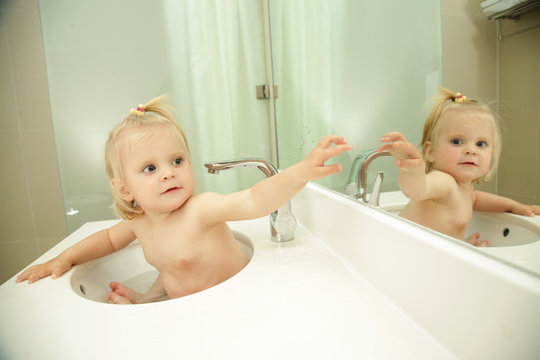 Cute blonde baby taking bath in bathroom sink