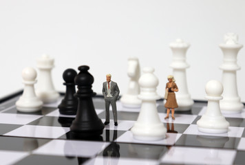 Miniature people standing and chess pieces on the chessboard.