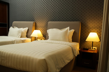 Modern generic bedroom interior, two single beds with clean white sheets and lamps on the nightstand