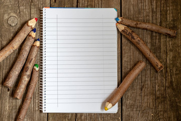 Pencils made of branches and a notebook on a wooden background