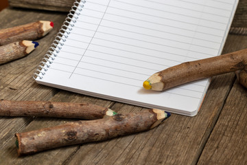 Pencils made of branches and a notebook on a wooden background