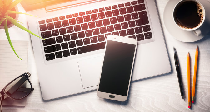 Smartphone und Laptop auf hellem Schreibtisch im Sonnenlicht