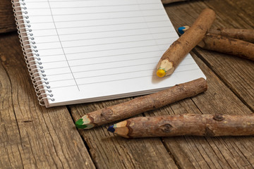 Pencils made of branches and a notebook on a wooden background